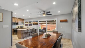Un'ampia sala da pranzo con tavolo e sedie in legno, una cucina con elettrodomestici moderni e una ventola a soffitto.