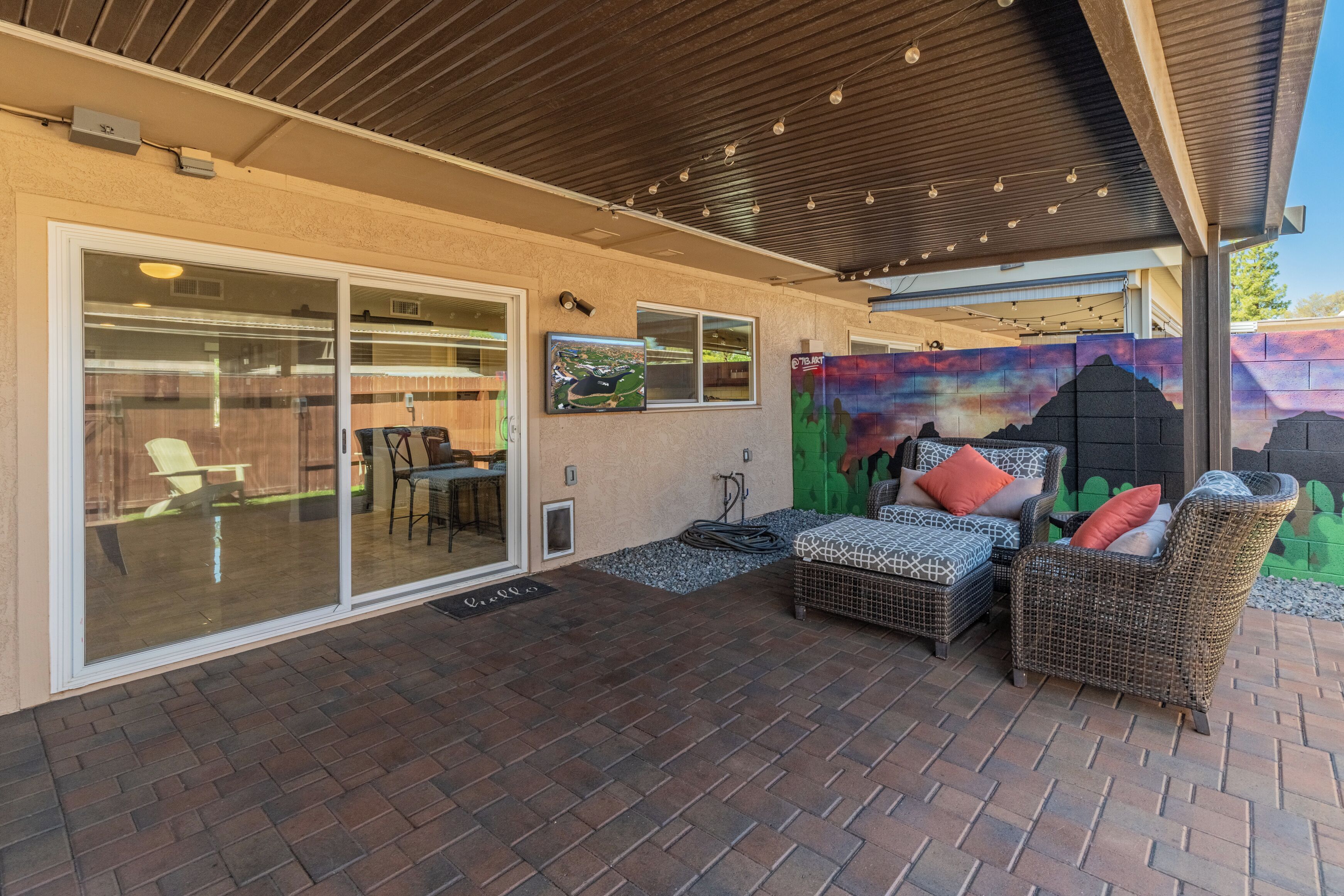A covered patio area with wicker furniture, a mural, and a sliding glass door leading to a patio.