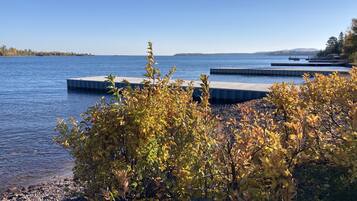 A lakeside view with a dock extending into the water, surrounded by autumn foliage and pebbles.