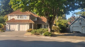 A two-story house with a garage, a driveway, and a large tree in front. - House in Bellevue (Bellevue)