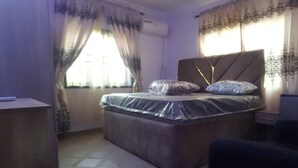 A bedroom with a bed, curtains, an air conditioning unit, and a patterned floor. - Have a Quality time with your Family in this  3bed apartment on the ground floor (Lagos)