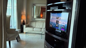 A modern hotel room with a large flat-screen TV, a sofa, a chair, and a dining table.