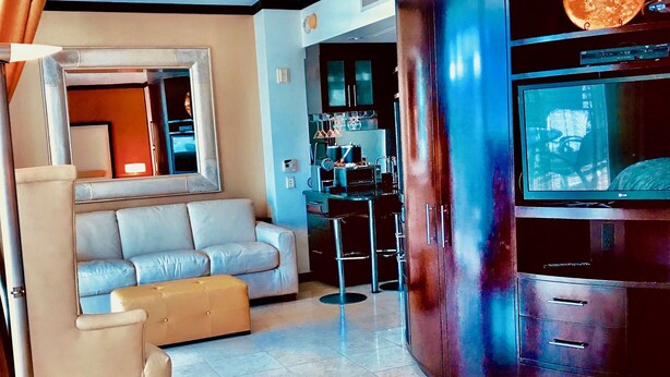 A modern hotel room with a large bed, a sofa, a dining area, and a TV.