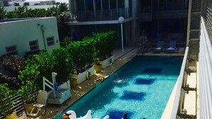 A rooftop pool with two swan inflatable floats, lounge chairs, and potted plants.