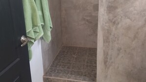 Een badkamer met een douche, betegelde vloer en groene handdoeken aan de deur.