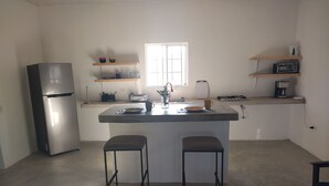 Een kleine keuken met een koelkast, een spoelbak, twee krukken en een raam.
