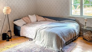 A bedroom with a bed, a floor lamp, a side table with a lamp, and a window with a view of trees. - Awesome home in Boxholm with WiFi (Boxholm)