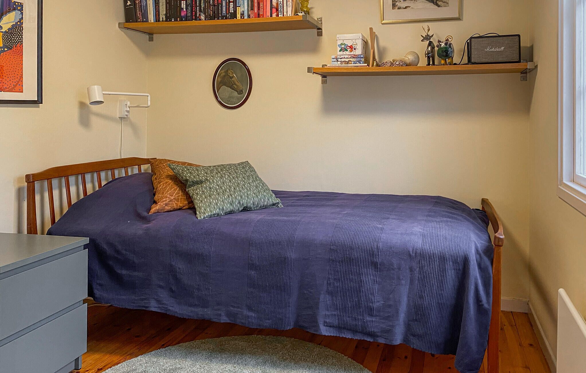A bedroom with a bed, a nightstand, a dresser, a bookshelf, and a radiator.
