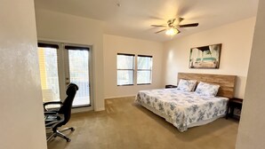 Un dormitorio con una cama, ventilador de techo, escritorio y dos ventanas.