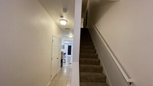 Un pasillo limpio y bien iluminado con una escalera alfombrada que conduce a otra habitación.