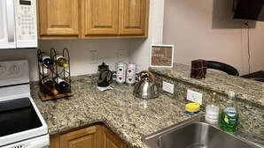 Una cocina con armarios de madera, un microondas, un hervidor y una cafetera. Hay un letrero en la pared que dice "Rise & Grind".