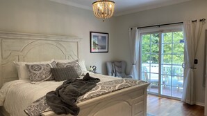 Un dormitorio con una cama grande, una araña de cristal, vistas al exterior a través de una puerta corrediza de vidrio y un cuadro en la pared.