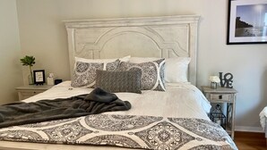 Una cama bien hecha con ropa de cama estampada, una mesita de noche con una planta y un cuadro en la pared.