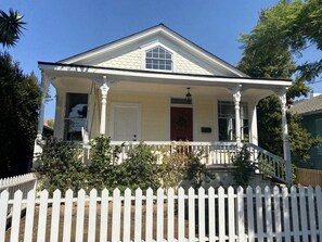 A two-story house with a white picket fence, a front porch, and a red door.