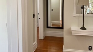 Un pasillo con suelo de madera, paredes blancas y una puerta que da a otra habitación.