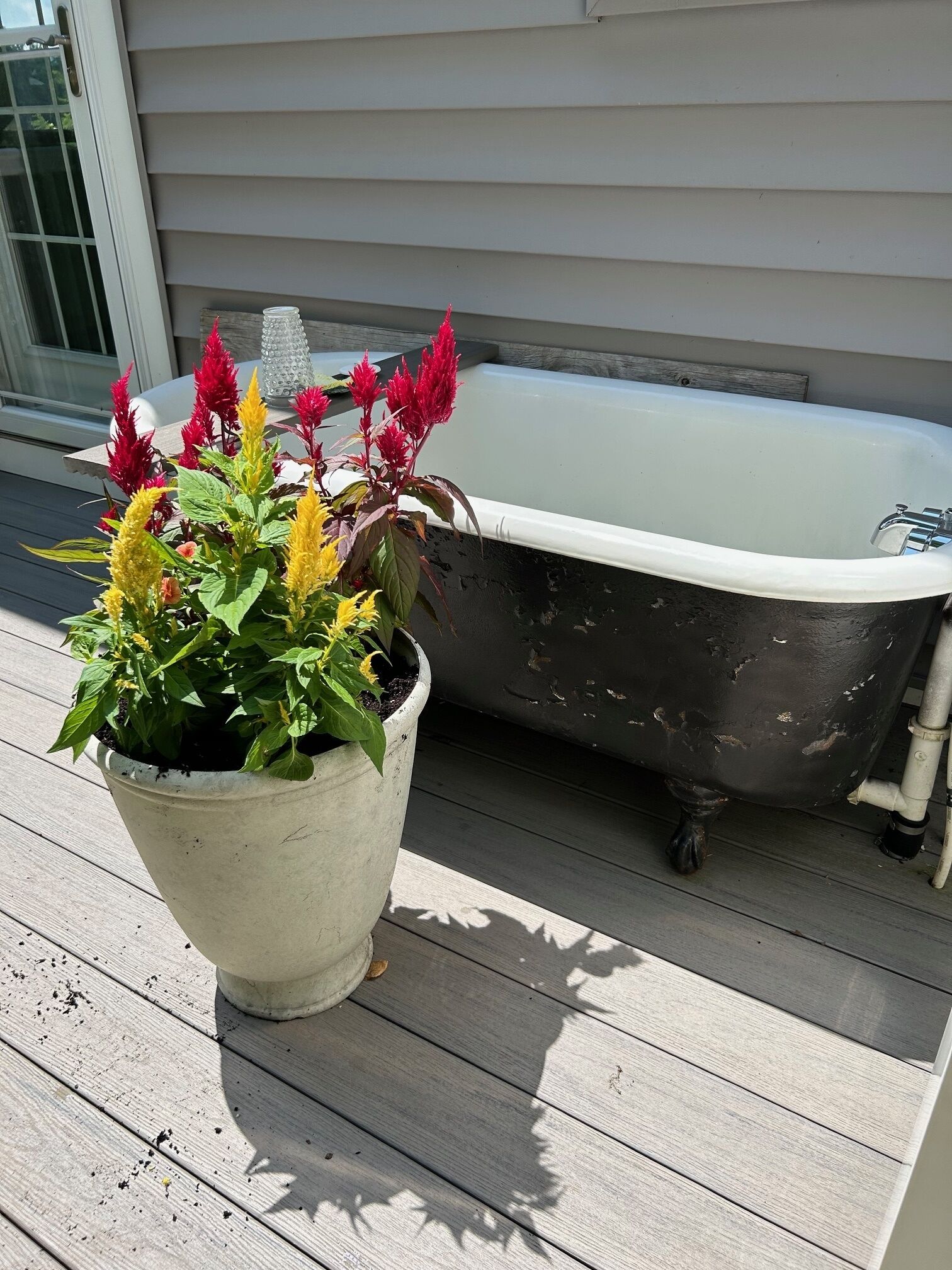 A white bathtub on a wooden deck next to a white planter with colorful flowers.