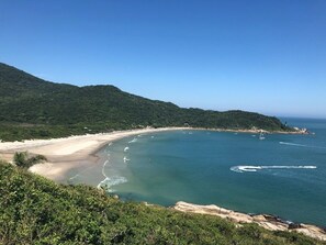 A coastal landscape with a beach, clear blue sea, and green hills. - Refúgio da Lagoinha do Leste (Pântano do Sul)