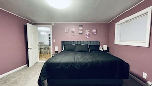 Ein Schlafzimmer mit einem Bett, einer Tür, einem Fenster und einer Wand mit Bildern.