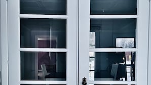 Eine weiße Doppeltür mit mehreren Glassfeldern, einem schwarzen Türgriff und dem Spiegelbild eines Raumes mit Tisch und Stühlen.