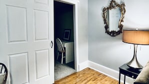 Ein Zimmer mit Holzboden, einer weißen Tür, einer schwarzen Lampe und einem Spiegel an der Wand.