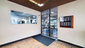 A hallway with a tiled floor, a glass door with a metal security gate, and a framed informational sign on the wall.