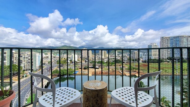 A balcony with two white chairs and a round table, overlooking a cityscape with buildings and a river.