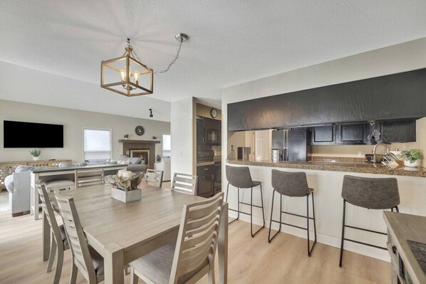 Una cocina moderna con una isla central, taburetes de bar y un comedor con una mesa y sillas de madera.