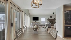 Une cuisine moderne dotée d’un four encastré, d’un coin repas avec une table et des chaises en bois, et d’une grande fenêtre agrémentée de rideaux.