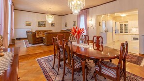 A spacious living room with a dining area, featuring a chandelier, wooden furniture, and a view into the kitchen.