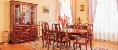 Een eetkamer met een houten tafel, zes stoelen, een grote houten kast en een kroonluchter.