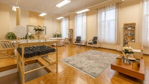 A spacious room with a wooden floor, a large rug, a desk with a chair, a bookshelf, and a window with curtains.
