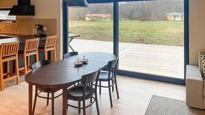 Une cuisine moderne dotée d’une grande fenêtre, de chaises en bois, d’une table à manger et offrant une vue sur un espace verdoyant avec des bâtiments visibles au loin.