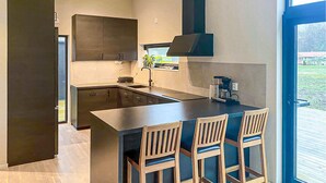 Une cuisine moderne avec des meubles de couleur sombre, un îlot central doté de tabourets de bar et une grande fenêtre offrant une vue sur l’extérieur.