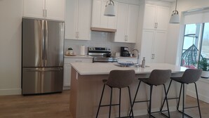 A modern kitchen with white cabinets, stainless steel appliances, a central island with bar stools, and pendant lighting.