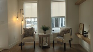 A living room with two white armchairs, a small round table, and a potted plant.