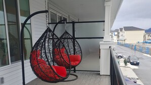 A balcony with two hanging chairs, a railing, and a view of parked cars and buildings in the background.