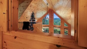 A wooden cabin with a sloped roof, a Christmas tree, and a view of the outdoors.