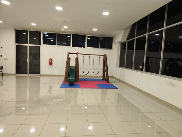 A spacious indoor area with a play area featuring a slide and swings, large windows, and a ceiling fan. - Apartamento Completo para 4 huéspedes (Panama City)