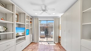 A hallway with white shelving, a ceiling fan, and a view to an outdoor patio with chairs.