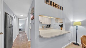 A modern kitchen with a 'WELCOME' sign, a countertop, cabinets, and a floor lamp.
