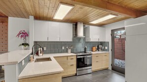 Een moderne keuken met houten balken, een groot kookeiland met spoelbak en uitzicht op een besneeuwde tuin.