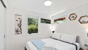 Een moderne slaapkamer met een groot bed, uitzicht op groen door ramen en een kunstwerk aan de muur.