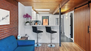 Een moderne keuken met witte kastjes, een houten plafond en twee zwarte barkrukken.