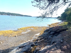 Kivikkoinen rantaviiva, kirkas vesi ja kaukainen maa.