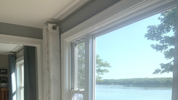 Une pièce dotée d’une grande fenêtre donnant sur un lac, d’un plancher en bois et d’une plante près de la fenêtre.