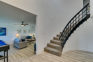 A modern living room with a staircase, wooden flooring, and a ceiling fan.