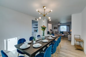 A modern dining area with a long table set for six, blue chairs, and a central vase with flowers.