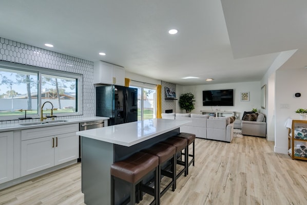 A modern kitchen with white cabinetry, a large island with stools, a built-in oven, and a window with a view of the outdoors.