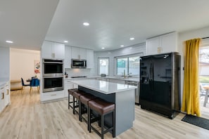 A modern kitchen with white cabinetry, a central island with bar stools, a black refrigerator, and a microwave.