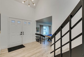 A spacious room with a wooden floor, a black staircase, and a pool table.